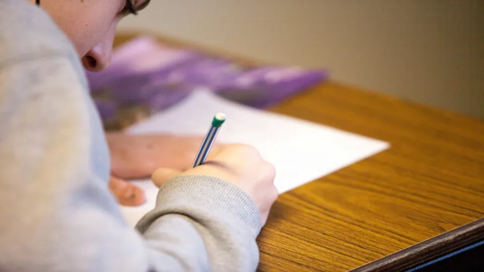 pessoa escrevendo em uma folha com lápis, avaliação educacional em ambiente escolar