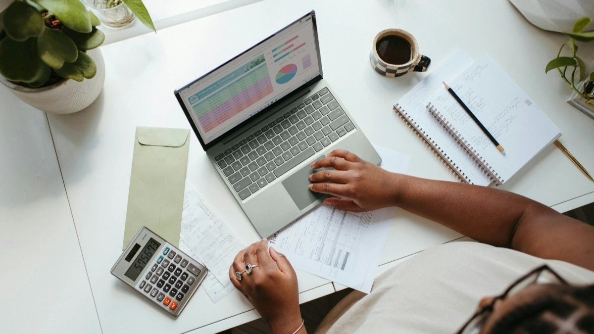 mulher mexendo no computador com uma calculadora e cadernos na mesa, pdi