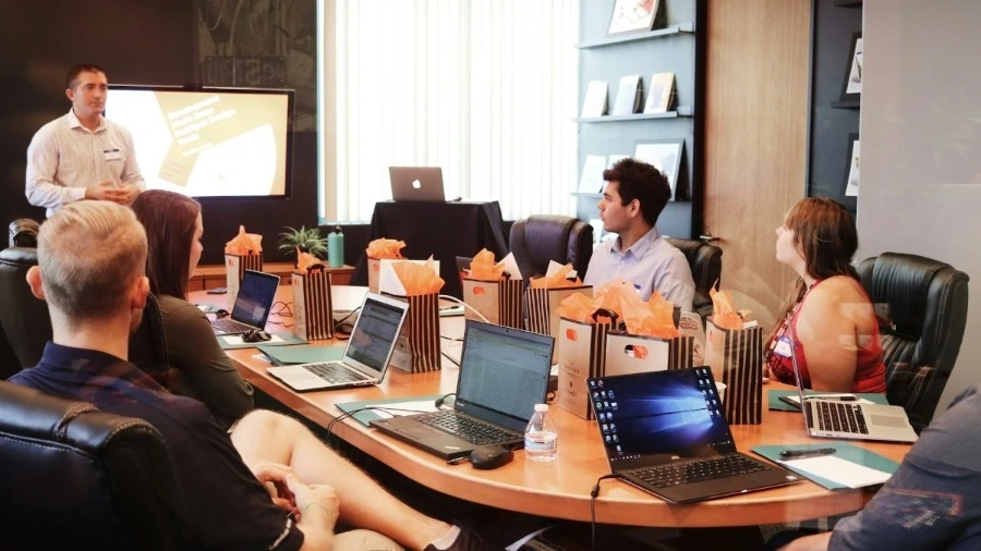 pessoas conversando em ambiente corporativo, notebooks na mesa, e uma televisão na sala, transformação digital