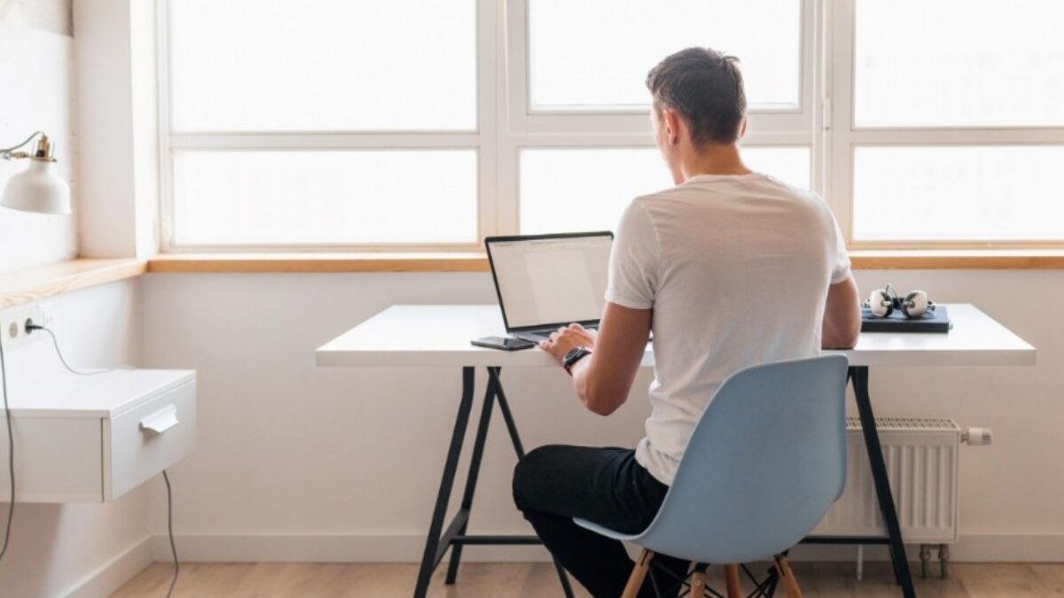 Homem jovem em roupa casual sentado à mesa trabalhando no laptop, trabalho remoto