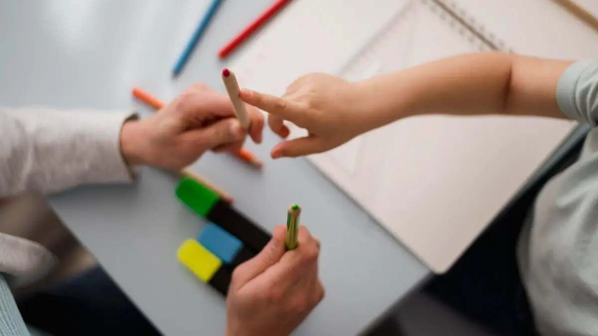 foto com foco nas mãos de um profissional ajudando um aluno com lápis de cor, psicologia escolar