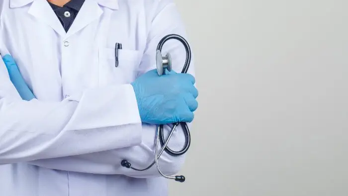 Médico cruzar os braços, mantendo o estetoscópio no jaleco branco, Enare