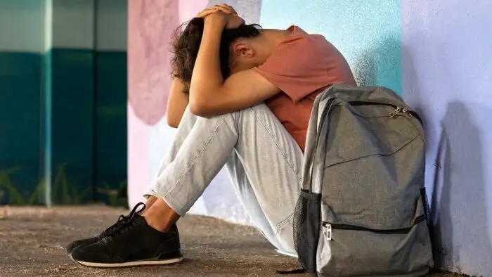 menino triste em escola sentado no chão, com mochila ao lado. reprovação escolar