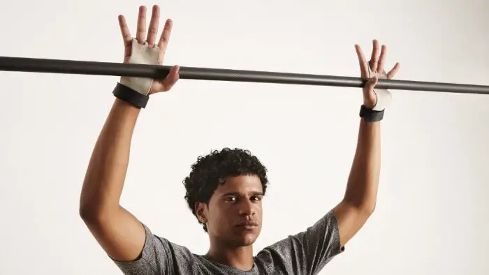 Ginasta negro de aparência séria em camiseta cinza e proteção de ginástica para as mãos se preparando para agarrar uma barra pullup de carbono preto, dedos estendidos. taf teste de aptidão física